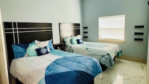 Een slaapkamer met twee bedden, een plafondventilator, een raam met zonwering en een marmeren vloer.