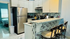 Een moderne keuken met witte kastjes, een roestvrijstalen koelkast, een marmeren aanrecht en een bar met stoelen.