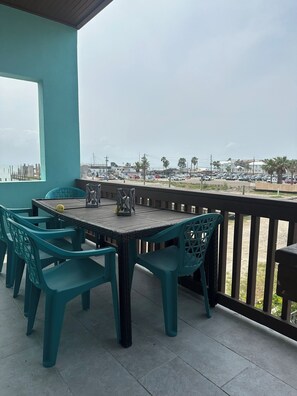 A covered outdoor seating area with a table and chairs, a view of the cityscape, and a railing. - Marisol Sunset Villas #254 (South Padre Island)
