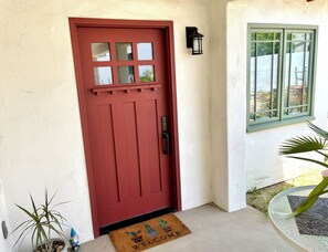 A red door with a window to the right, a welcome mat, and a potted plant. - Comfy guest house with AC in sunny North Hollywood! (Los Angeles)
