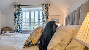 Ein Schlafzimmer mit Bett, Vorhängen, einem Fenster, einem Kopfteil und einem Gemälde.
