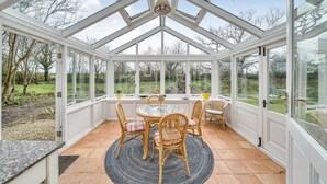 Ein Wintergarten mit Glasveranda, einem runden Tisch, Korbstühlen und Blick auf den Garten.