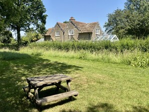 Ein Steinhaus mit einem großen Rasen, einem Holz-Picknicktisch und einem Gewächshaus.