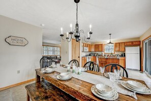A dining area with a wooden table set for four, surrounded by chairs. A chandelier hangs above, and a sign on the wall reads 'HOME is where the heart is.' - Ski/family/kids/fully-stocked kitchen/spacious (Coolbaugh Township)