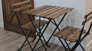 Puisesta pöydästä ja tuoleista koostuva kokonaisuus, seinälle kiinnitetty hylly, jossa on kuppeja, sekä liukuva, navetan tyylinen ovi.