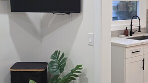 Moderni keittiö, jossa on valkoiset kaapit, musta työtaso, ruukkukasvi ja seinälle asennettu litteänäyttöinen televisio.