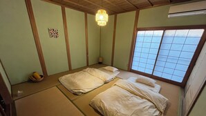 A traditional Japanese room with tatami flooring, two beds, a hanging light fixture, and a window with a grid pattern. - Guesthouse Riad Camellia (Mitoyo)