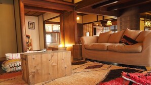 A traditional Japanese-style living room with tatami mats, a low wooden coffee table, and a beige sofa with cushions. - Guesthouse Riad Camellia (Mitoyo)