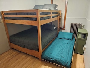 Een stapelbed met een onderbed, een eenpersoonsbed en een klein groen kastje.