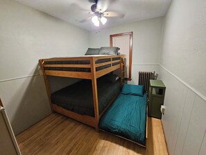 A small, single-bedded room with a wooden bunk bed, a radiator, and a ceiling fan.