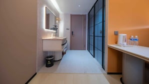 Un pasillo de hotel con un baño moderno, un cubo de basura y una mesa con agua embotellada y una tetera.