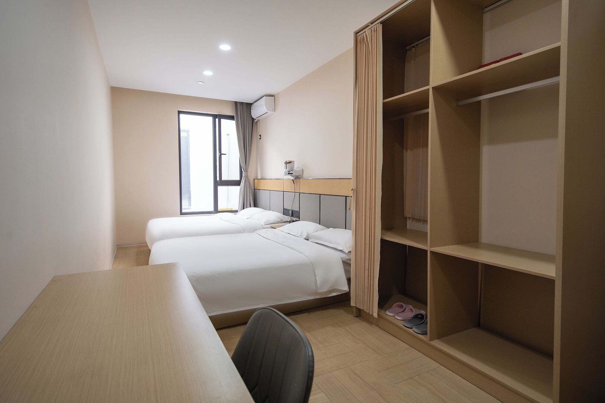 Une chambre d’hôtel avec deux lits, un bureau, une chaise, une armoire et une fenêtre.