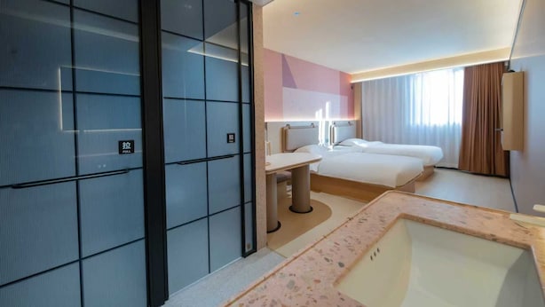 Habitación de hotel con una cama grande, un escritorio, una silla y un baño con lavamanos, además de una puerta corredera.