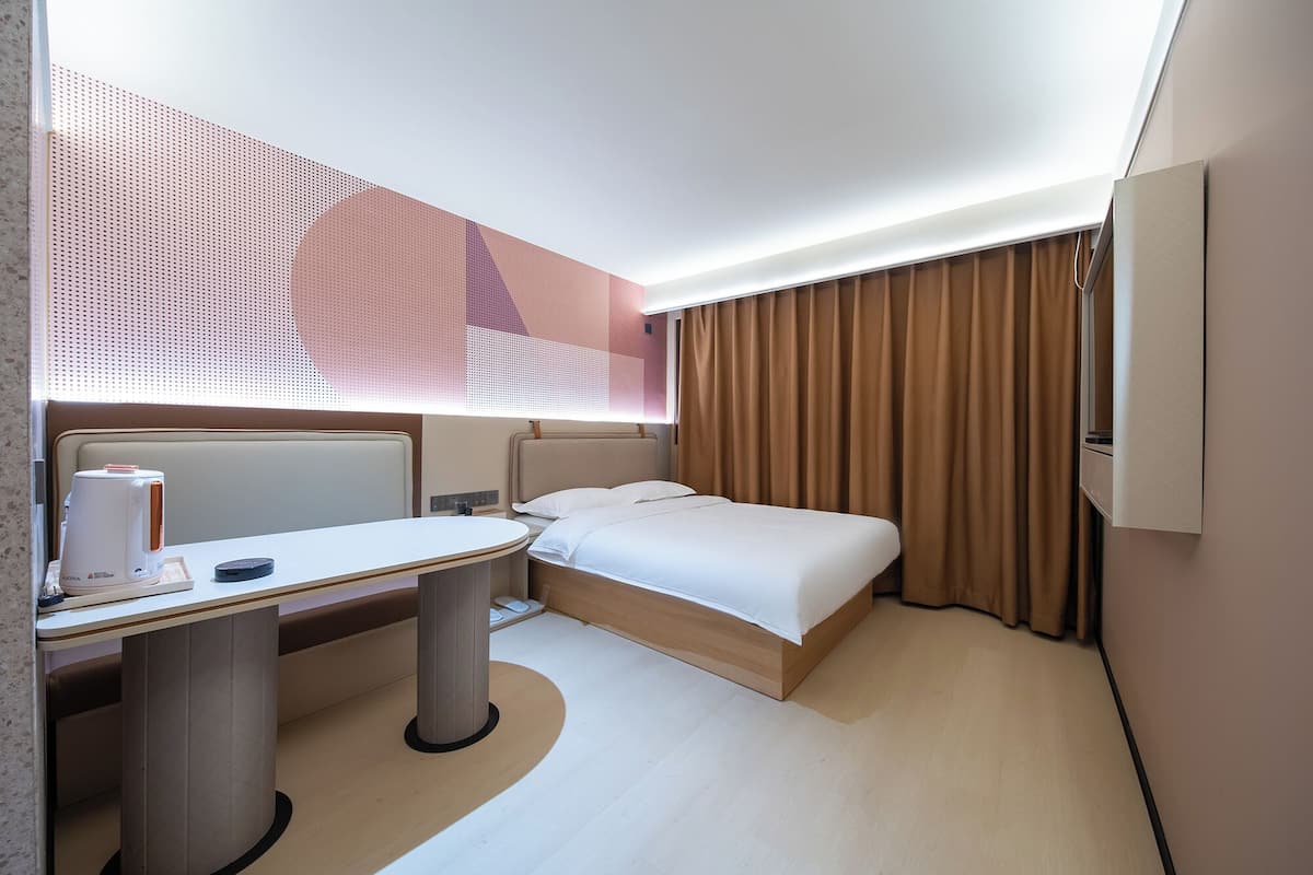 Moderni hotellihuone, jossa on sänky, yöpöytä ja työpöytä tuolilla.