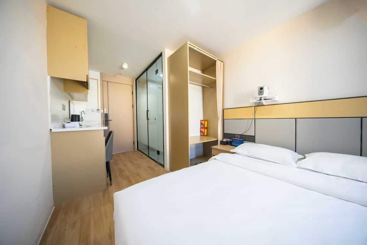 Hotellihuone, jossa on sänky, työpöytä, vaatekaappi ja liukuovilla varustettu kaappi.