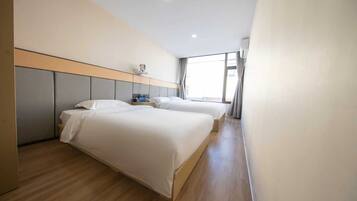 Une chambre d’hôtel avec deux lits, un plancher en bois, une tête de lit, une fenêtre avec des rideaux et un luminaire au plafond.