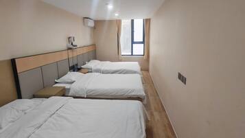 A hotel room with three beds, a bedside table, a window, and a wall-mounted air conditioning unit.