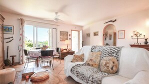 A cozy living room with a white sofa, a dining table with chairs, a ceiling fan, and a large window. - Villa vue mer au calme (SAN GIULIANO)