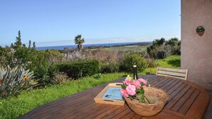 A wooden deck with a table, a basket of flowers, and a bottle. - Villa vue mer au calme (SAN GIULIANO)