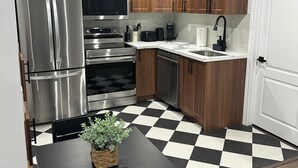 Une cuisine moderne dotée d’appareils électroménagers en acier inoxydable, de meubles de rangement en bois, d’un carrelage à motifs et d’une table à manger noire.