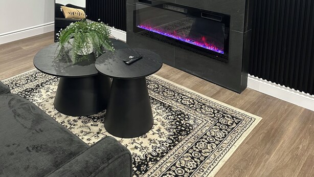 Un salon moderne doté d’une cheminée, d’un grand téléviseur à écran plat, d’un miroir et d’une table basse ronde agrémentée de plantes décoratives.