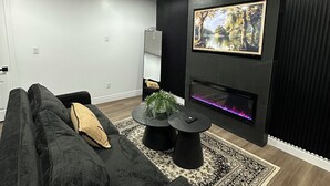 Un salon moderne avec un canapé noir, une cheminée, un téléviseur fixé au mur et un tapis à motifs.