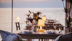Ett matbord dukat med tallrikar, bestick, glas och en lampa, med utsikt över havet.