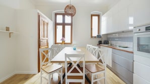 Een moderne keuken met witte kasten, een houten eettafel met witte stoelen en een hangende lamp.