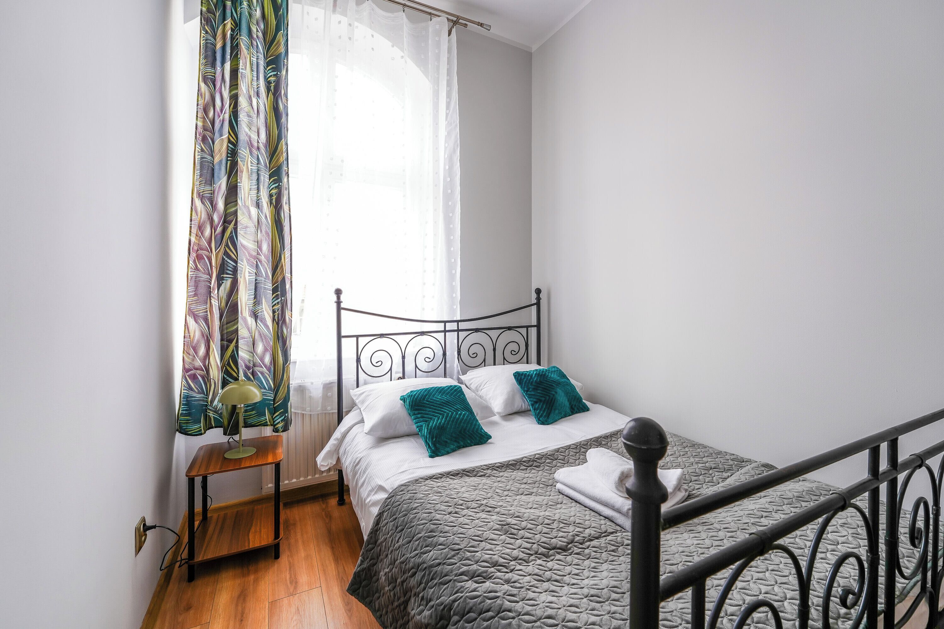 Une chambre à coucher avec un lit, une table de chevet, une lampe, une fenêtre avec des rideaux et un radiateur.