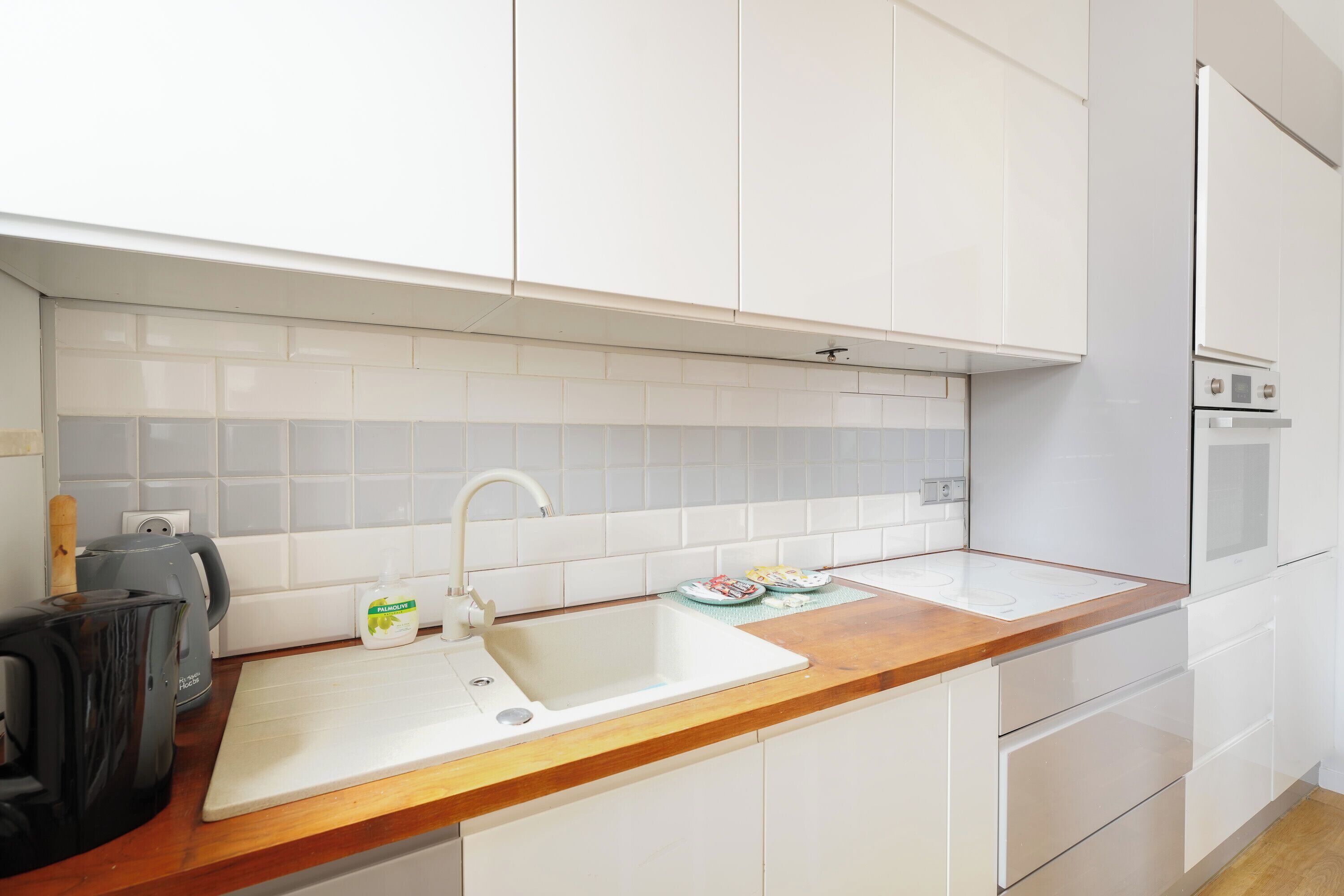 A modern kitchen with white cabinets, a wooden countertop, a double sink, and a built-in oven.