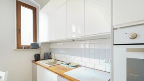 Een kleine keuken met witte kastjes, een houten aanrecht, een inbouwoven en een raam boven de spoelbak.
