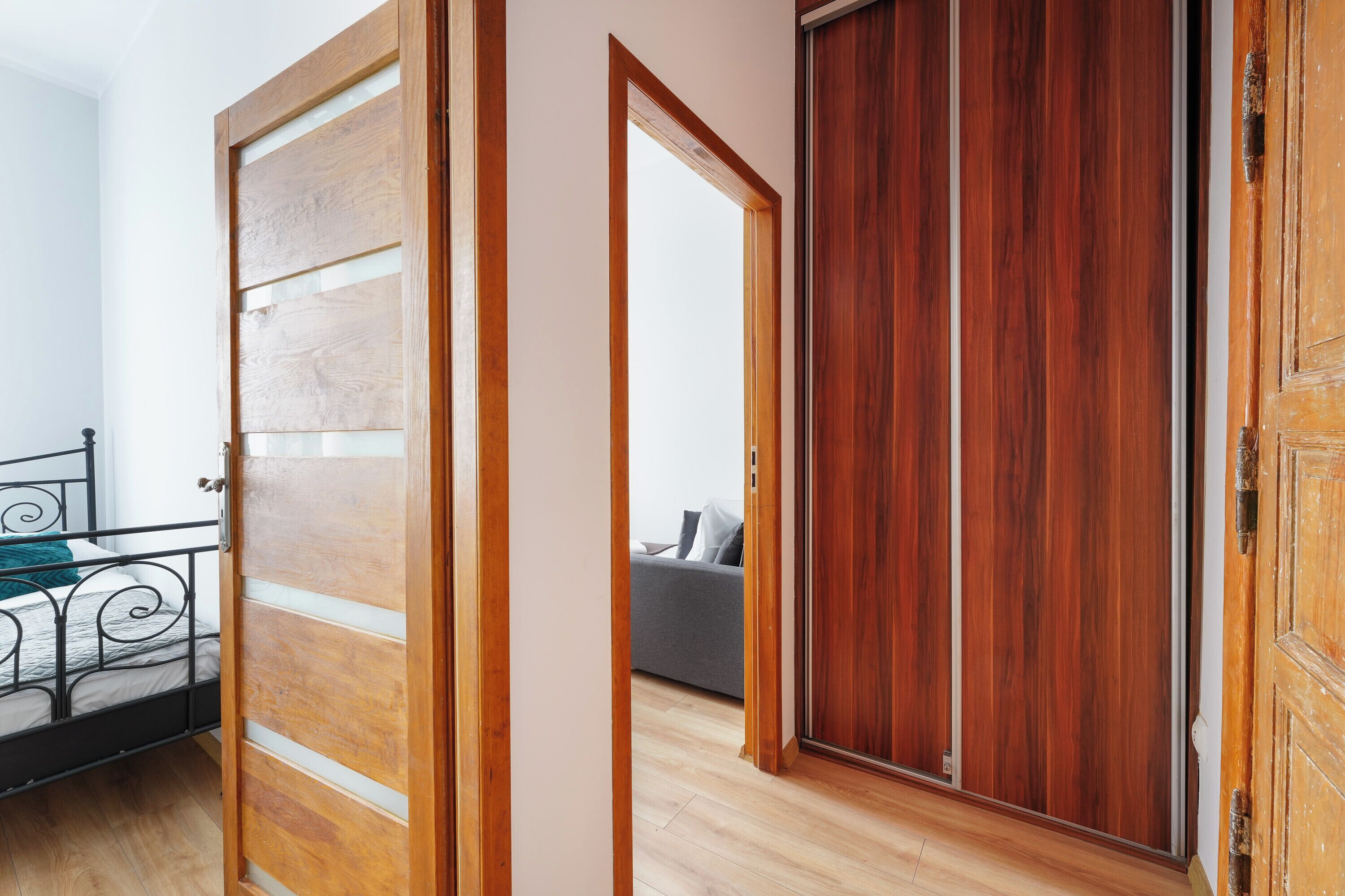 A bedroom with a bed, a wooden door, and a view into another room.