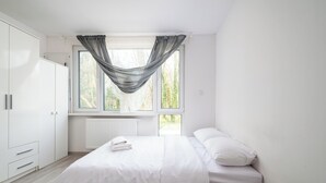 Makuuhuone, jossa on sänky, ikkuna verhoilla, patteri ja vaatekaappi.