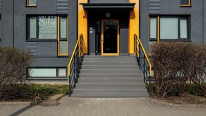 Moderni rakennus, jossa on portaikko, joka johtaa mustalle ovelle. Ovi on ympäröity pensailla.