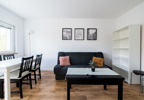 A modern living room with a black sofa, a dining table with chairs, a coffee table, and a white bookshelf. - Grunwald Płomienna Apartment (Poznań)
