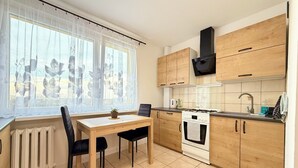A modern kitchen with wooden cabinets, a stove, and a dining table with chairs. - Bystrzycka Comfort Apartment (Wrocław)