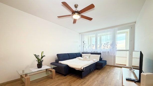 A bedroom with a bed, a ceiling fan, a window, and a bedside table. - Bystrzycka Comfort Apartment (Wrocław)