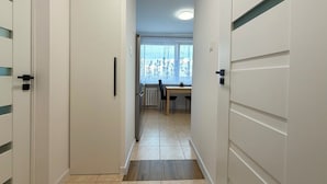 A hallway leading to a dining area with a table and chairs, a radiator, and a window with curtains. - Bystrzycka Comfort Apartment (Wrocław)