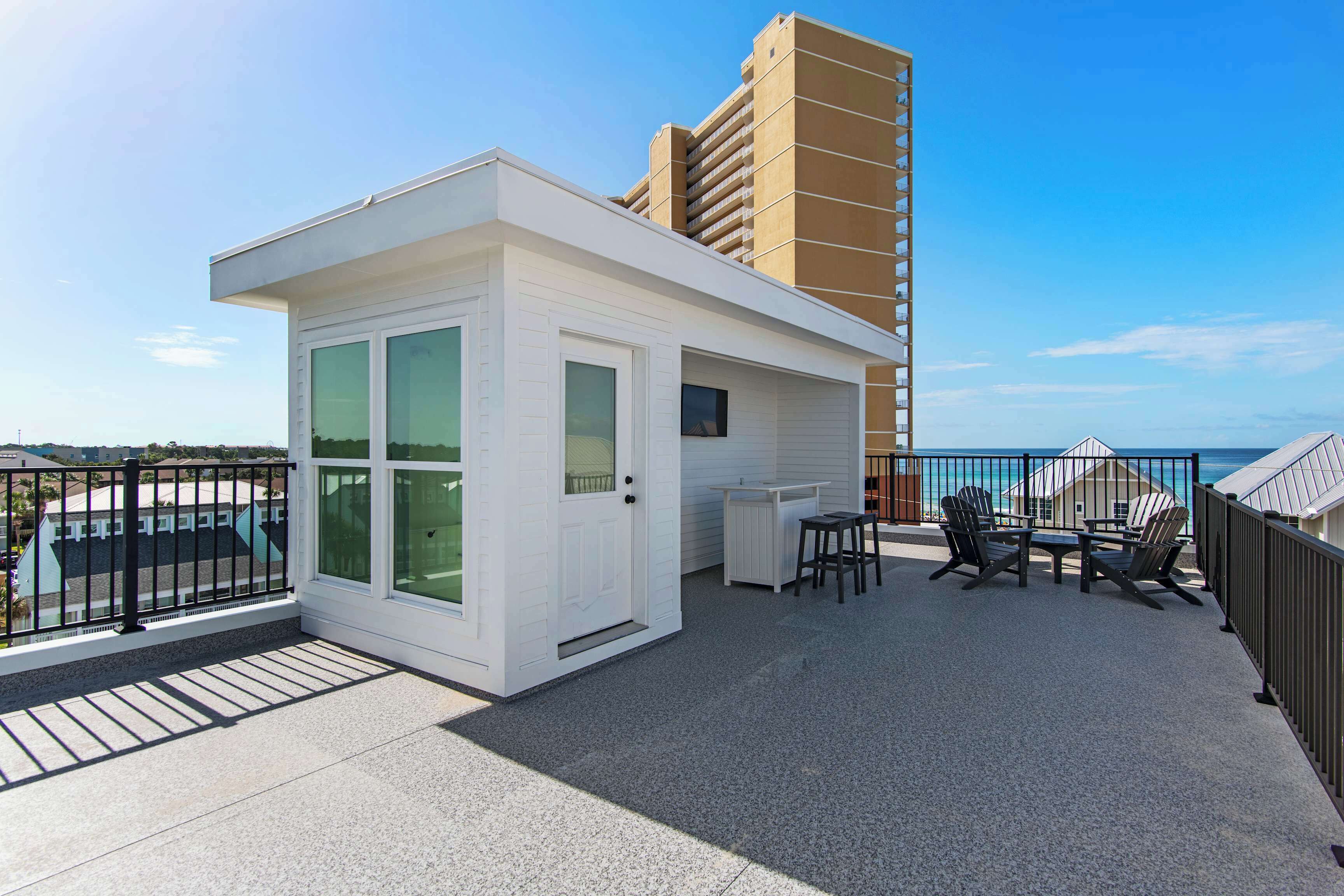 Spacious rooftop terrace with modern white structure, featuring ocean views, comfortable seating area, and outdoor dining space perfect for seaside relaxation.