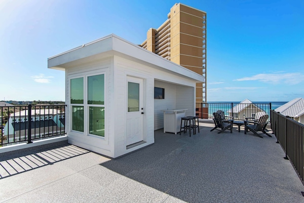 Spacious rooftop terrace with modern white structure, featuring ocean views, comfortable seating area, and outdoor dining space perfect for seaside relaxation.