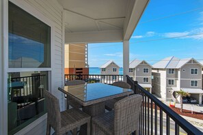 Ein Balkon mit Korbmöbeln, einem Glastisch und Blick auf KĂŒstengebĂ€ude.