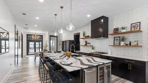 A modern kitchen with a central island, bar stools, stainless steel appliances, and decorative shelves. - Poole Party! Incredible Pool, Beachside of 30A (Seagrove Beach)