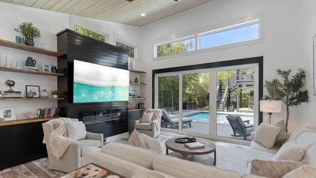 A modern living room with a flat-screen TV, comfortable seating, a fireplace, and a view of a pool. - Poole Party! Incredible Pool, Beachside of 30A (Seagrove Beach)
