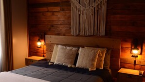 Une chambre à coucher aux murs lambrissés, avec un lit, deux lampes de chevet, une décoration murale en macramé et un tapis à motifs.