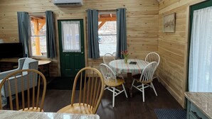 A cozy cabin interior with a dining area, wooden walls, and a sloped ceiling. - Cozy Woodland Cabin Living with Loft and Brookside Views (Boscawen)