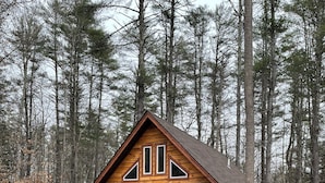 A wooden cabin with a porch, a front door, and a small front yard. - Cozy Woodland Cabin Living with Loft and Brookside Views (Boscawen)