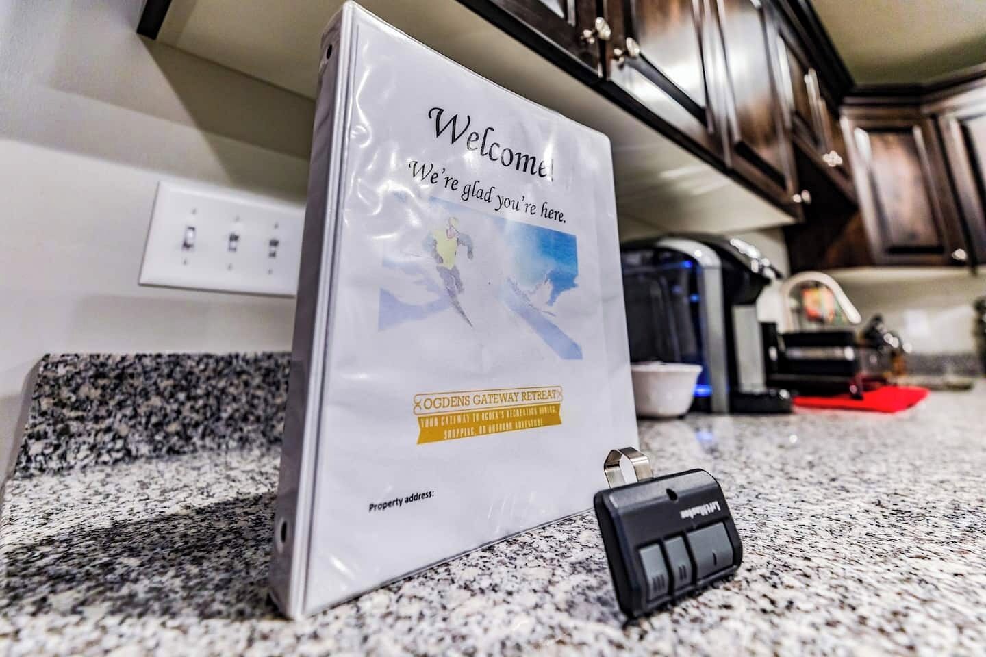 A welcome sign in a kitchen with a granite countertop and dark wooden cabinets.