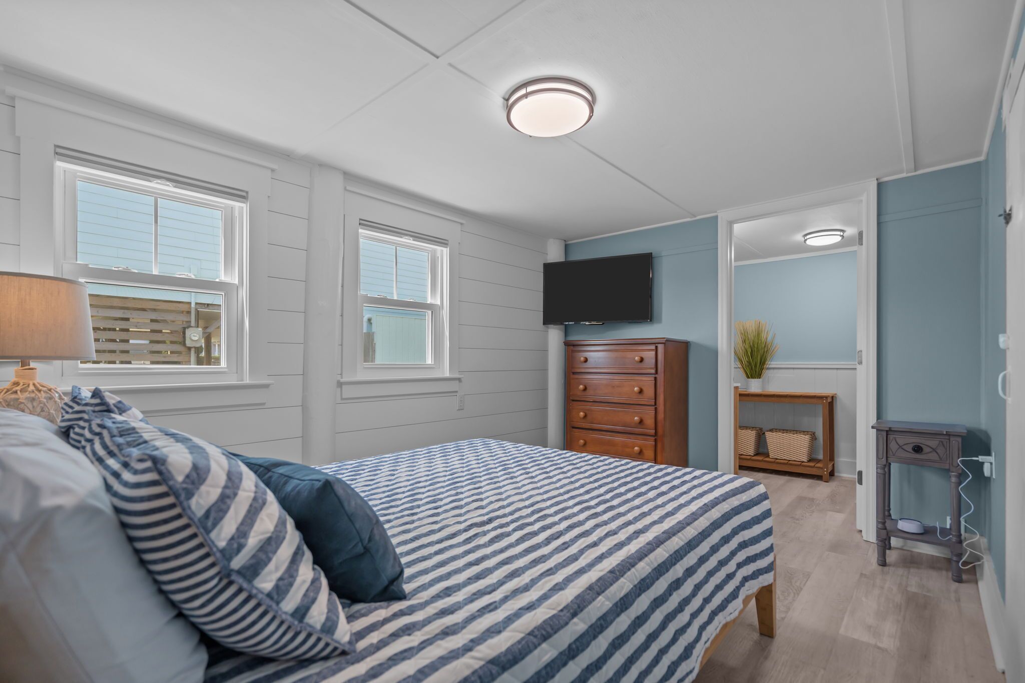 A bedroom with a bed, dresser, television, and a small table with a plant.