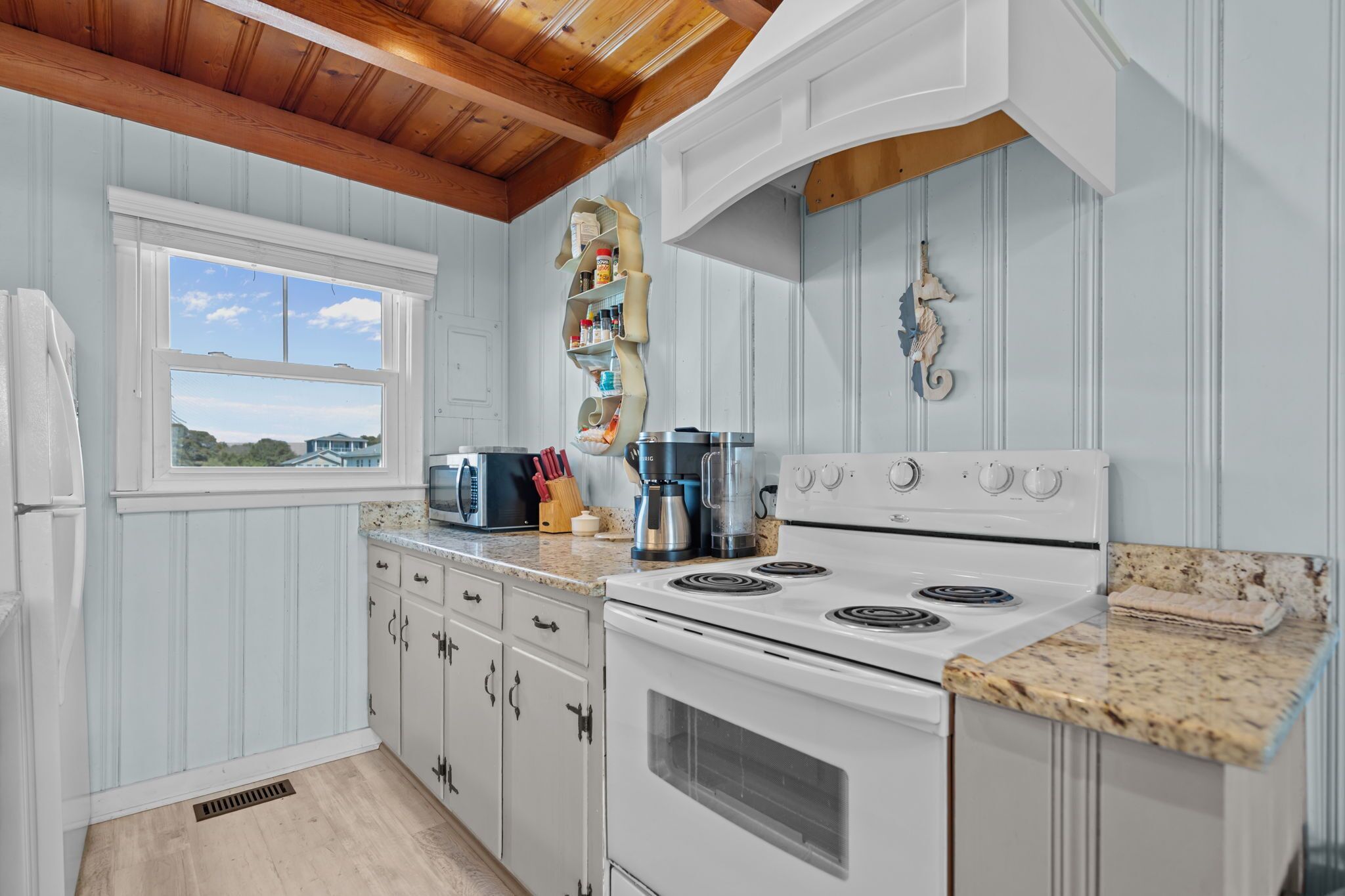 Una cocina con armarios blancos, estufa, microondas y ventana con vistas.