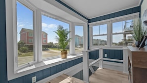 A room with large windows, a wooden floor, and a view of neighboring houses.